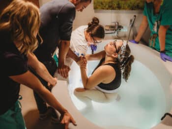 Midwife Paige, a VBAC provider, assists mom delivering in the water at Poudre valley hospital in fort collins co